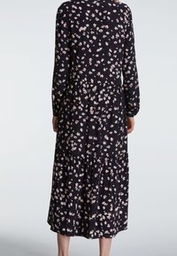 Czarna sukienka w kwiaty z długimi rękawami, z warstwowym krojem i małymi różowymi oraz białymi wzorami kwiatowymi. Miękka tkanina, luźny krój.