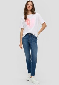 Camiseta gráfica blanca con un diseño de corazón rosa, combinada con jeans ajustados azul y zapatillas blancas. Un atuendo simple y casual.