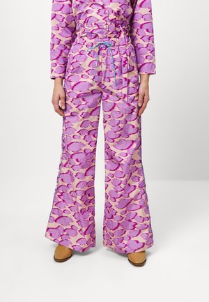 Persona que lleva pantalones de pierna ancha de talle alto con un diseño abstracto en rosa y púrpura y cordón azul, combinados con zapatos marrones.