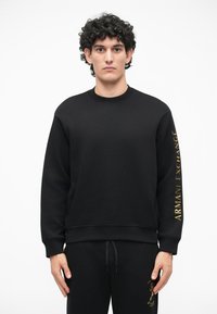 Melnas kokvilnas sporta krekls ar apaļu kakla izgriezumu un ribu aprocēm. Kreklam ir zelta "ARMANI EXCHANGE" teksts kreisajā piedurknē. Maiga tekstūra.