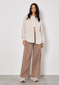 Beige textured button-up top with long sleeves, paired with taupe wide-leg trousers. Footwear features light and dark tones.