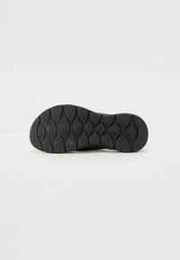 Black rubber outsole featuring a textured surface with various oval and circular patterns. Designed for traction and durability.