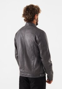 Grå läderjacka med en slät yta, med en ståkrage, sidosömmar och tryckknappsstängning nederst, sedd bakifrån.