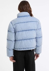 Lichtblauwe pufferjack met horizontale stiksels, hoge kraag en elastische zoom. Getextureerde stof met blauwe accenten en cropped ontwerp.