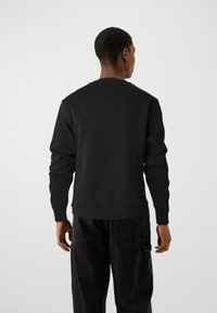 Svart crewneck sweatshirt, bomullsblandning, ribbad mudd och fåll, minimalistisk design, bakvy visar slät textur och rena linjer.