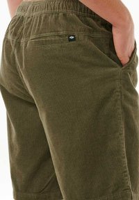 Olijfgroene ribfluweel short met een gestructureerd ribpatroon, voorzien van een elastische tailleband en zijzakken voor functionaliteit.