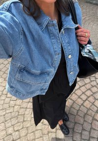 Vaaleansininen farkkutakki, jossa on rento leikkaus, kaksi etutaskua ja hopeiset napit, yhdistettynä mustaan mekkoon ja matalapohjaisiin mustiin kenkiin.