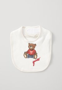 White cotton bib featuring a bear graphic in red sweater and blue jeans, with "guess" embroidered in red, along the bottom edge.