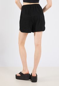 Black, textured shorts with a pleated design and elastic waistband. Paired with chunky black platform sandals.