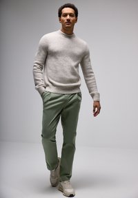 Light gray wool sweater with a round neckline and ribbed cuffs, paired with green chinos and beige sneakers. The design is simple and modern.