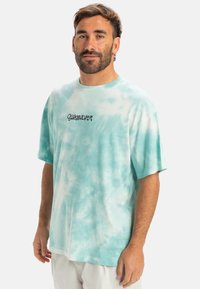 Light blue tie-dye t-shirt made of cotton with a round neck and short sleeves; features a black "Quiksilver" logo on the front.