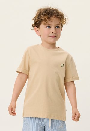 Beige cotton t-shirt with a round neckline, rolled sleeves, and green embroidered "II" detail on the chest, worn with striped shorts.