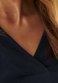 Tissu bleu marine avec une texture lisse, présentant un design en V et des détails de couture. Les ombres mettent en valeur les contours du col.