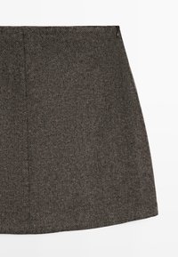 Brun A-formet nederdel med sildebensmønster og en lynlås i siden, vist mod en hvid baggrund.