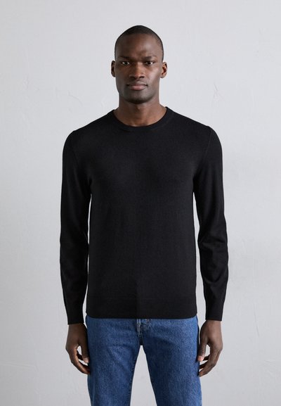 Pull noir à manches longues avec un col rond, fabriqué à partir d'un matériau doux et lisse ; associé à un jean en denim bleu.
