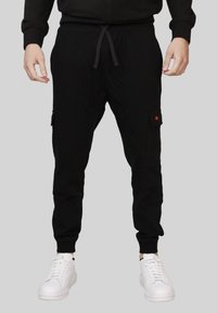 Joggers cargo neri in tessuto morbido, con vita elasticizzata e cordoncino, tasche laterali e polsini affusolati. Abbinati a sneakers bianche.