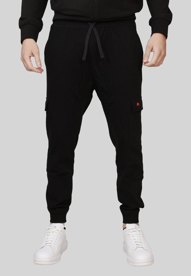 Joggers cargo neri in tessuto morbido, con vita elasticizzata e cordoncino, tasche laterali e polsini affusolati. Abbinati a sneakers bianche.
