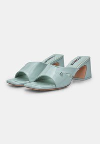 Mint green patent leather mules with an open toe, angular block heel, and crossed strap design. Smooth texture and minimalistic hardware.