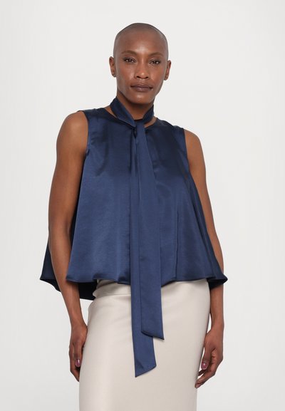 Navy satin sleeveless blouse with a tie neckline, flared silhouette, and smooth texture, paired with a light beige fitted skirt.