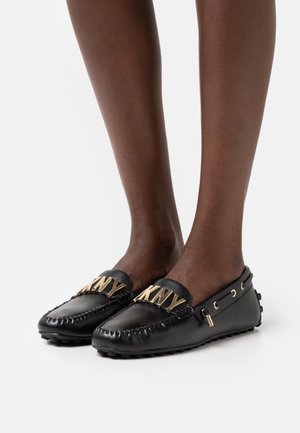 Chaussures de style mocassin en cuir noir avec logo doré, couture décorative et semelle en caoutchouc. Comprend des accents latéraux et un bout arrondi.
