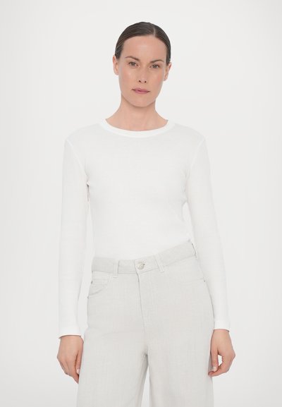 White long-sleeve fitted top made of lightweight fabric, with a round neck and smooth texture, paired with light gray high-waisted pants.