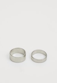 Två metallringar på en vit bakgrund; en är bredare med en matt yta, den andra är smalare med en slät yta, båda silverfärgade.