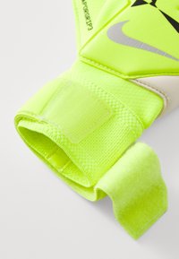Neon sárga kapuskesztyű, textúrált anyaggal, tépőzáras záródással, fehér és fekete kiegészítőkkel, ergonómikus kialakítással a jobb fogás érdekében.