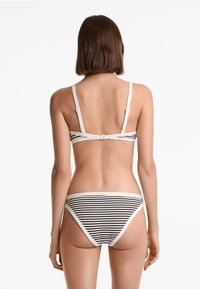 Kvinna med kort brunt hår som bär vit och svart randig bikiniunderdel och en matchande bikinitopp, sedd bakifrån.