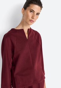 Burgundia värvi pullover, V-kaelusega, külgõmblustega ja pikkade varrukatega. Pehme kangas siledas tekstuuris ja vabalt langev istuvus.