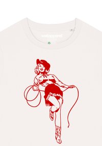 Cremfarbener T-Shirt mit einer roten Illustration einer Frau mit einem Lasso, die einen Hut und Cowboy-Stiefel trägt und fransige Shorts hat.