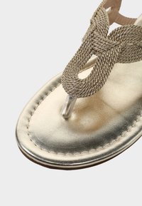 Goldmetallische Sandale mit geflochtenem Riemendesign. Verfügt über eine flache Sohle und einen transparenten Zehensteg. Glatte Textur und abgerundete Form.