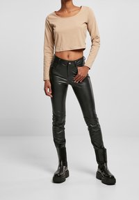 Beige langärmliges Cropped-Top kombiniert mit engen schwarzen Lederhosen und klobigen schwarzen Stiefeln, die glatte Texturen und körpernahe Silhouetten zur Schau stellen.