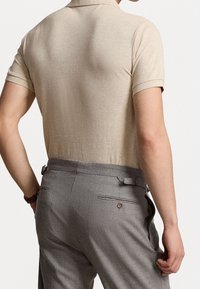 Camisa polo beige con un patrón texturizado, con mangas cortas. Combinada con pantalones gris ajustados con bolsillos y un detalle de cinturón.