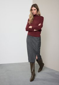 Bordo spalvos golfas, pilkas languotas pieštuko formos sijonas su šoniniu plyšiu ir rudi batai iki kelių. Lygus audinys su prigludusia silueto linija.