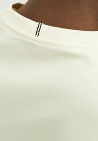 Tricou din bumbac de culoare verde deschis, cu guler rotund și un accent de cusătură neagră. Textură moale cu țesătura vizibilă.
