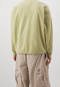 Ljusgrön fleece-tröja med långa ärmar, avslappnad passform och utan synliga knäppningar, tillsammans med beige cargobyxor med sidofickor.