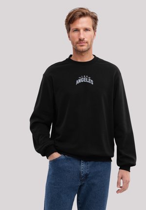 Black sweatshirt with ribbed cuffs and neckline, featuring "L.O.S. ANGELES" embroidered in white. Worn with blue denim jeans.