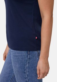 Mørkeblå kortærmet top med en glat tekstur, der har et lille rødt accent ved kanten, og som er sat sammen med lyseblå denimjeans.