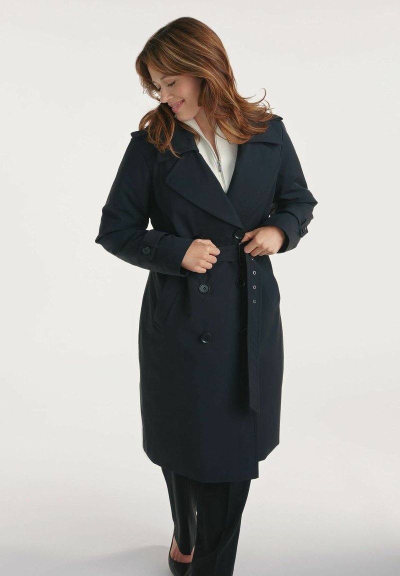 Granatowy płaszcz trench z podwójnym zapięciem, dużymi klapami i paskiem w talii. Posiada ozdobne guziki i kieszenie boczne. Gładki, sztywny materiał.