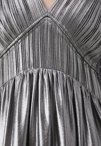 Robe argent métallique avec des plis verticaux, un décolleté en V et une texture froncée à la taille, créant un effet de jupe fluide.