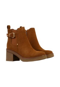 Bottines en velours marron avec un talon carré, fermeture éclair sur le côté et sangle décorative avec une boucle en métal. Texture lisse et design à bout rond.