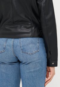Black leather jacket with smooth texture and fitted design, paired with mid-rise blue denim jeans featuring classic back pockets.
