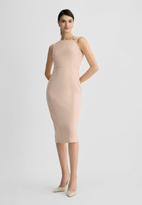 Růžové těsné šaty s lodními výstřihem a elegantními ramínky. Hladká textura, délka po kolena, v kombinaci s béžovými zdobenými vysokými podpatky.