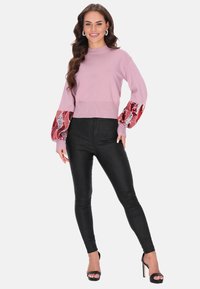 Różowy sweter z dzianiny z cekinowymi czerwonymi i srebrnymi bufiastymi rękawami, w połączeniu z czarnymi obcisłymi spodniami i czarnymi butami na obcasie z odkrytymi palcami.