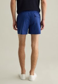Shorts a righe blu realizzati in tessuto leggero, con vita elastica e tasca posteriore. Indossati con sneakers bianche.