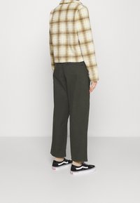 Rutigt gult och brunt jacka, lösa olivgröna byxor och svarta sneakers med vita accenter. Enkelt mönster och texturerad tyg.