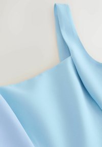 Vêtement sans manches bleu clair avec une large bretelle et une texture de tissu lisse.