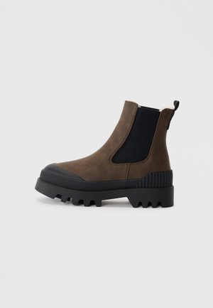 Brune lær ankle boot med elastiske sider, sort gummisål og ribbede accenter. Har en dragtap for nem påtagning og en tekstureret overflade.