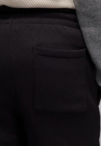 Pantaloni scurți din țesătură neagră cu buzunar lateral, talie elastică și textură moale. Cusături vizibile și un articol vestimentar superior stratificat, de culoare gri.