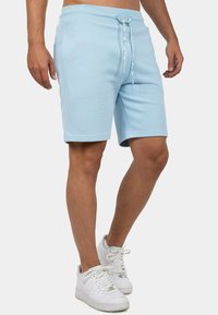 Shorts de sport bleu clair avec une taille élastique, un cordon de serrage et des poches latérales, fabriqués en tissu coton doux. Assortis à des baskets blanches.